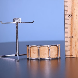 May include: A miniature drum set with a wooden drum and a silver stand. The drum is about 2 inches in diameter and has a natural wood finish. The stand is made of metal and has a tripod base.