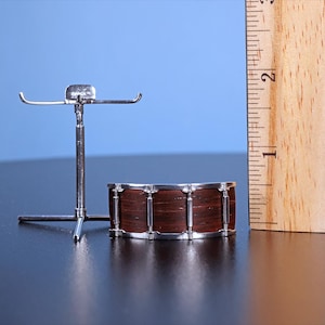 May include: A miniature drum set with a brown wooden drum and a silver metal stand. The drum is about 2 inches in diameter.