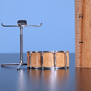 May include: A miniature drum set with a wooden drum and a silver stand. The drum is about 2 inches in diameter and has a natural wood finish. The stand is made of metal and has a silver finish.