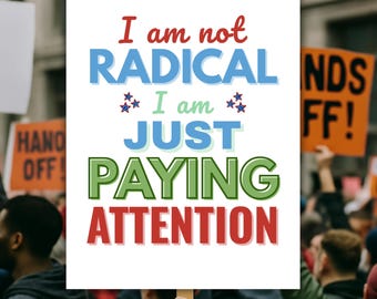 May include: A white sign held up in a crowd with the words "I am not RADICAL I am JUST PAYING ATTENTION" in red, blue, green, and white. The sign is held up in a crowd of people, with other signs visible in the background.