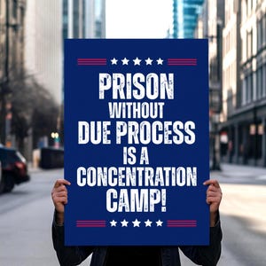 May include: A blue poster with white text that reads "PRISON WITHOUT DUE PROCESS IS A CONCENTRATION CAMP!" The poster has red and white star accents. The image is taken outdoors with a blurred city background.