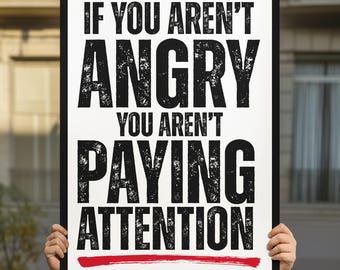 Pode incluir: Um cartaz com moldura preta com o texto "IF YOU AREN'T ANGRY YOU AREN'T PAYING ATTENTION" em negrito, fonte preta desgastada. Uma linha vermelha sublinha o texto. A pessoa que segura o cartaz está vestindo uma camiseta amarela.