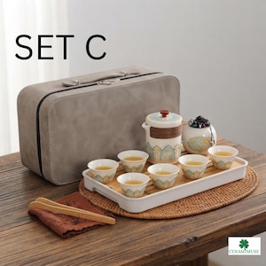 Könnte beinhalten: Ein Teeservice mit der Aufschrift SET C, bestehend aus einer weißen Keramik-Teekanne mit blau-goldenem Muster, sechs passenden kleinen Teetassen, einem runden Behälter mit Deckel und einem weißen rechteckigen Tablett mit Bambuseinsatz in einem grauen Koffer.