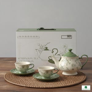 May include: A ceramic tea set featuring a teapot and two teacups with matching saucers, all decorated with a delicate green floral pattern. The set is displayed in front of a white and green box labeled Afternoon Tea Collection.