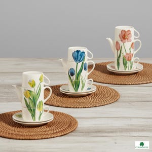 May include: Stacked teacups and teapots with floral tulip designs in yellow, blue, and pink. Each set includes a saucer. The teacups and teapots are stacked on top of each other. The sets are arranged on round woven placemats.