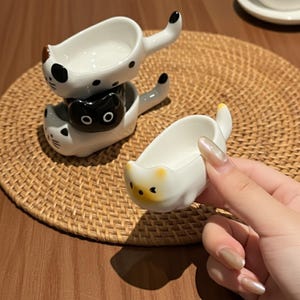 Puede incluir: Un juego de tres tazas de cerámica con un acabado moteado y mate. Las tazas son de color crema, marrón claro y marrón oscuro. Cada taza tiene un diseño simple y minimalista.