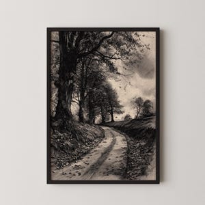 May include: Black and white framed art print of a winding dirt road through a forest. Tall trees line the road, with fallen leaves scattered on the ground. The sky is overcast, creating a moody, vintage aesthetic.