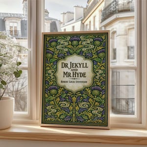 Op de afbeelding: Een ingelijste prent van "Dr. Jekyll and Mr. Hyde" van Robert Louis Stevenson. Het kunstwerk toont een groen, paars en geel bloemmotief rond de titel in een crèmekleurige ovaal. De lijst heeft een lichte houtkleur.