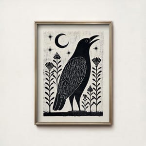 May include: Black and white art print of a raven with an open beak, set against a cream-colored background. The raven is surrounded by stylized plants, stars, and a crescent moon. The artwork is framed in a gold-colored frame.