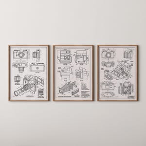 Op de afbeelding: Set van drie ingelijste prints met gedetailleerde blauwdrukken van vintage camera's. Elke print toont verschillende cameramodellen, met explosietekeningen en technische diagrammen in zwart-wit, tegen een neutrale achtergrond. De frames zijn van warm, natuurlijk hout.