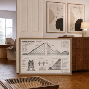 May include: A framed architectural print titled Riverbend Roller Coaster, featuring a detailed black line drawing of a wooden roller coaster structure on a light beige background, including technical diagrams, cross-sections, and structural notes.