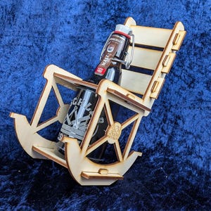 Könnte beinhalten: Ein kleiner Schaukelstuhl aus hellem Holz, der zwei Flaschen hält. Der Stuhl hat ein klassisches Design. Die Flaschen sind dunkel mit Etiketten und Metallverschlüssen. Der Hintergrund ist ein strukturiertes blaues Gewebe.