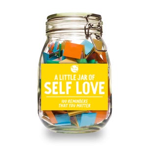 May include: A glass jar filled with colorful paper slips, with a yellow label that reads "A Little Jar of Self Love 100 Reminders That You Matter".