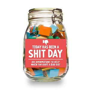 以下が含まれることがあります： カラフルな紙切れでいっぱいのガラス瓶。赤いラベルには「TODAY HAS BEEN A SHIT DAY 100 AFFIRMATIONS TO HELP WHEN YOU HAVE A BAD DAY」と書かれています。