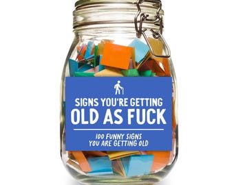 Puede incluir: Un tarro de vidrio lleno de papeles de colores, etiquetado con "Signs You're Getting Old as Fuck". La etiqueta también dice "100 Funny Signs You Are Getting Old".