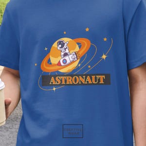 Bonita camiseta de astronauta con cohete: divertida caricatura espacial con planetas y estrellas, perfecta para niños, regalos de cumpleaños o amantes de la ciencia ficción kawaii.