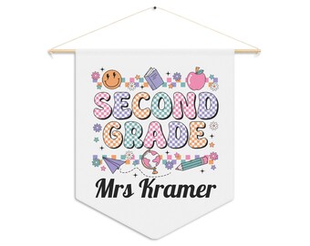 Pode incluir: Uma faixa branca com uma vara de madeira e barbante para pendurar. A faixa apresenta as palavras "SECOND GRADE" em letras coloridas em estilo retrô, juntamente com o nome "Mrs Kramer" em uma fonte de script. O design inclui um smiley, uma maçã e um lápis.