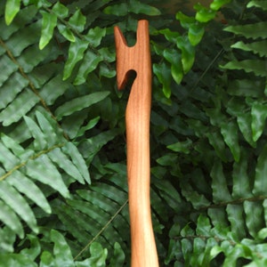 May include: A wooden crochet hook with a unique curved handle. The hook is made of natural wood and has a smooth finish.