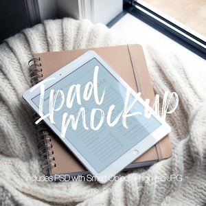 May include: A white tablet with a light blue screen displaying a checklist, resting on a brown notebook and a spiral-bound notebook. The text "iPad mockup" is overlaid on the tablet. The background includes a cream-colored knitted blanket.