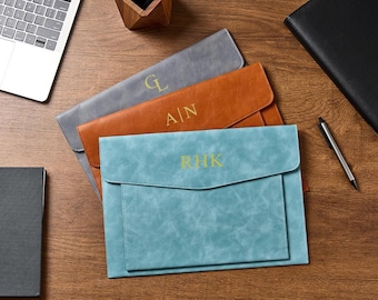 May include: Three rectangular document folders in light blue, tan, and gray, each featuring a flap closure and gold-colored monogrammed initials. The blue folder is embossed with RHK, the tan folder with A|N, and the gray folder with GL.