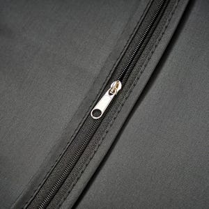 May include: A close-up view of a dark gray fabric surface featuring a central black zipper closure. The zipper track is integrated into the material with a silver-toned metal pull tab positioned vertically along the center of the textile panel.