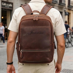 May include: A brown leather backpack featuring a top handle, two adjustable shoulder straps, and multiple zippered compartments. The front of the bag is embossed with the name Jeanne in a cursive script, and it includes side pockets.
