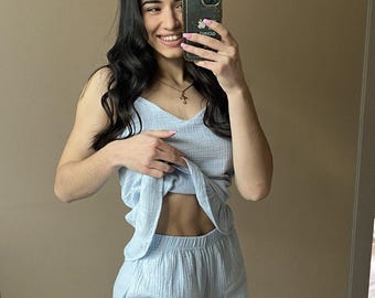 Puede incluir: Conjunto de pijama de dos piezas azul claro. El conjunto incluye una camiseta sin mangas y pantalones cortos con dobladillo con volantes. La tela tiene un aspecto texturizado y arrugado. La persona de la imagen sostiene un teléfono.