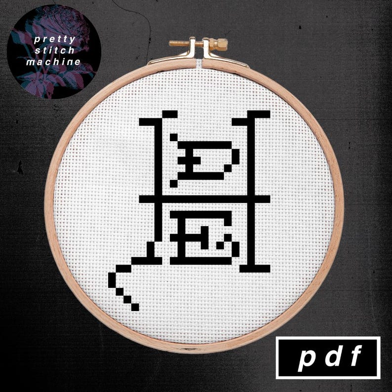 Op de afbeelding: Een kruissteekontwerp in een houten borduurring. Het ontwerp heeft een zwarte gepixelde afbeelding met de letters "H" en "E" en een gebogen lijn. De tekst "pretty stitch machine" staat in een cirkel linksboven en "pdf" rechtsonder.