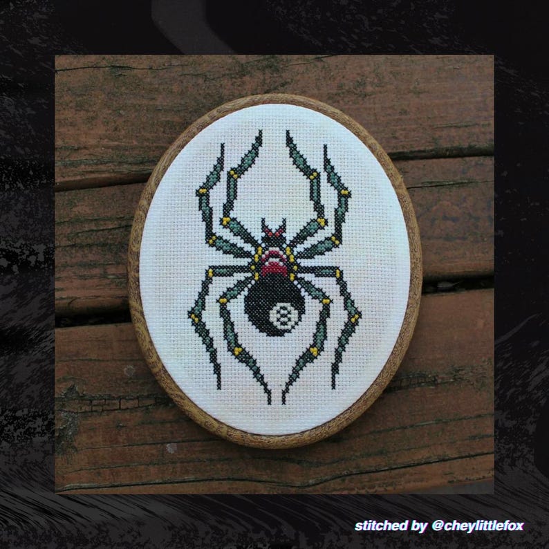 Puede incluir: Punto de cruz ovalado con una ara&ntilde;a negra con un abdomen de bola ocho. La ara&ntilde;a tiene detalles verdes y amarillos en sus patas y una cabeza roja. El punto de cruz est&aacute; en un marco de madera. El texto "stitched by @cheylittlefox" est&aacute; en la parte inferior.