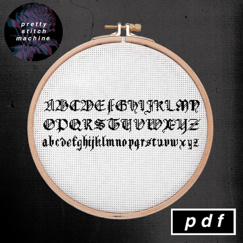 May include: A cross-stitch pattern for an alphabet in a black gothic font. The pattern is displayed in a wooden embroidery hoop on a black background. The text "pdf" is displayed in a white rectangle at the bottom of the image.