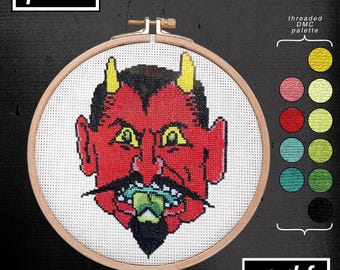 May include: A cross-stitch embroidery of a red devil face with yellow horns, a black mustache, and a green tongue. The embroidery is set in a wooden hoop. The image includes the text "psm" and "pdf". A color palette is also shown.
