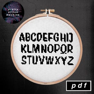 K&ouml;nnte beinhalten: Ein schwarz-wei&szlig;es Kreuzstichmuster des Alphabets in einer pixeligen Schriftart. Das Muster ist in einem h&ouml;lzernen Stickrahmen auf schwarzem Hintergrund dargestellt. Der Text "pdf" ist in einem wei&szlig;en Rechteck auf schwarzem Hintergrund dargestellt.