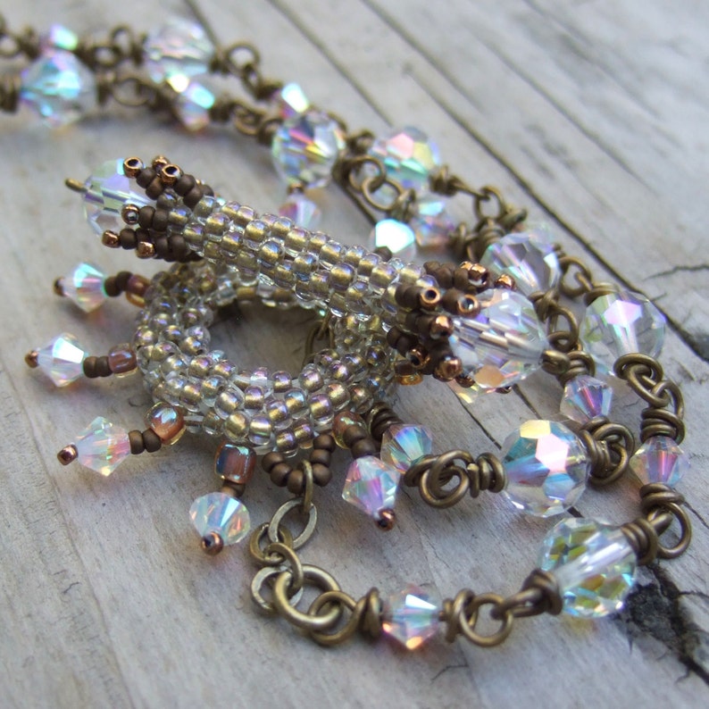 K&ouml;nnte beinhalten: Eine Perlenkette mit schillernden Glasperlen und einer braunen Metallkette. Die Kette hat einen Perlenanh&auml;nger mit einem Spiralmuster.