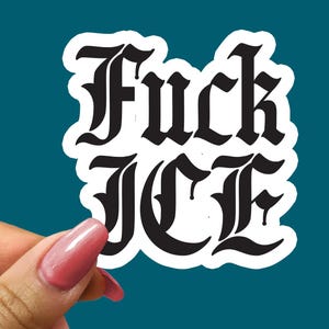 May include: A white sticker with the words "Fuck ICE" in a black gothic font. The sticker is held by a hand with pink nail polish against a teal background.
