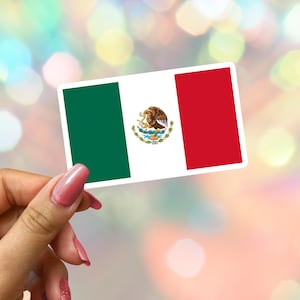 Könnte beinhalten: Ein rechteckiger Aufkleber mit der mexikanischen Flagge. Die Flagge hat drei vertikale Streifen: grün, weiß mit dem Wappen und rot. Der Aufkleber wird von einer Hand gehalten, mit einem verschwommenen Hintergrund.