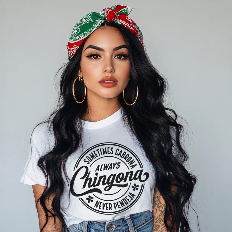May include: A white t-shirt with a black circle graphic that says "Sometimes Cabrona Always Chingona Never Pendeja". The model is wearing a red and green bandana and large hoop earrings.