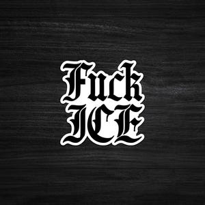 May include: A white sticker with the words "Fuck ICE" in a gothic font. The sticker is on a dark wood grain surface.