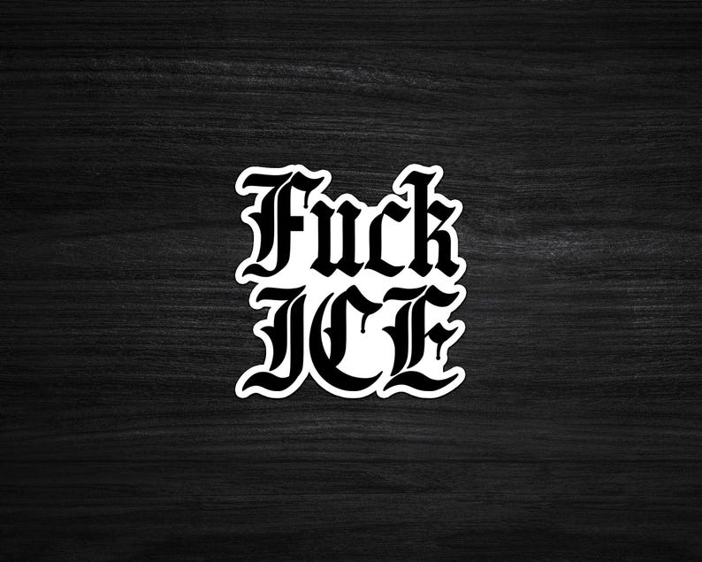 May include: A white sticker with the words "Fuck ICE" in a gothic font. The sticker is on a dark wood grain surface.