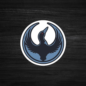 May include: A circular sticker featuring a stylized bird with outstretched wings. The bird is primarily navy blue with light blue accents and a red eye, set against a white background. The design is enclosed within a light blue border.