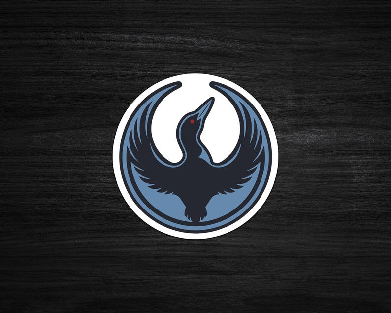 May include: A circular sticker featuring a stylized bird with outstretched wings. The bird is primarily navy blue with light blue accents and a red eye, set against a white background. The design is enclosed within a light blue border.