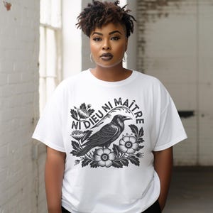 May include: White t-shirt with a black and white graphic of a crow with flowers and the text "NI DIEU NI MAÎTRE".