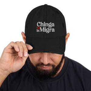 以下が含まれることがあります： 白の「Chinga la Migra」の刺繍と赤いバラが特徴の、黒のダメージ加工ベースボールキャップ。キャップは、あらかじめカーブしたバイザーと使い古したような外観をしています。