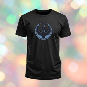 May include: Black t-shirt featuring a blue circular design with a bird emblem. The bird is depicted with outstretched wings inside a circle. The t-shirt is made of a soft material and has short sleeves.