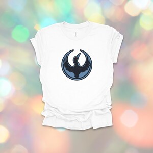 May include: White t-shirt featuring a dark blue bird emblem within a circular frame. The bird design has a stylized, minimalist aesthetic. The shirt is made of a soft material and has a classic crew neck.