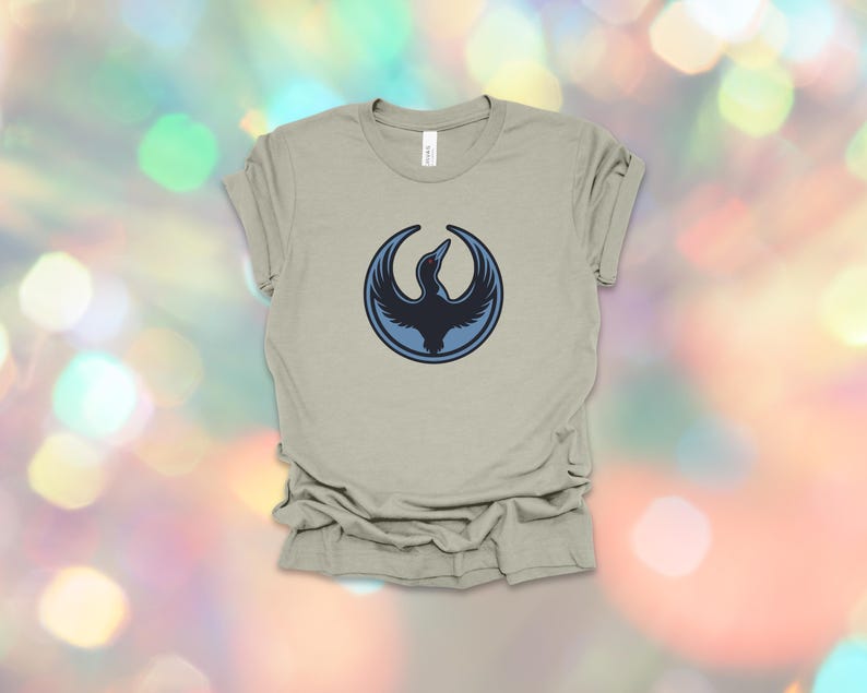 May include: A light olive green t-shirt featuring a circular design with a dark blue bird graphic. The bird is in flight, with its wings spread. The shirt is made of a soft material and has a classic crew neck.
