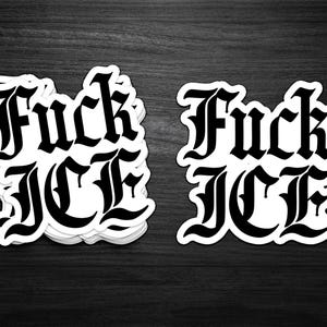 May include: Black and white stickers with the phrase "Fuck ICE" in a gothic font. The stickers are stacked on a dark wooden surface. The text is bold and easily readable.