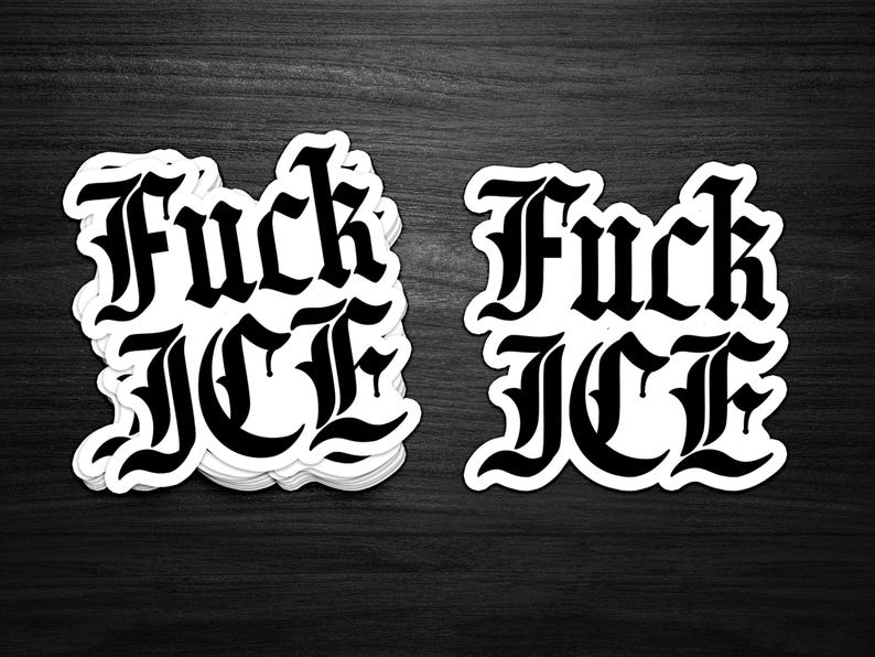 May include: Black and white stickers with the phrase "Fuck ICE" in a gothic font. The stickers are stacked on a dark wooden surface. The text is bold and easily readable.