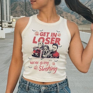 Puede incluir: Camiseta sin mangas color crema con un gráfico de Halloween. El gráfico presenta el texto "GET IN LOSER" sobre una imagen de Jason Voorhees, Ghostface y Michael Myers en un coche. El texto "We're going slashing" está debajo.