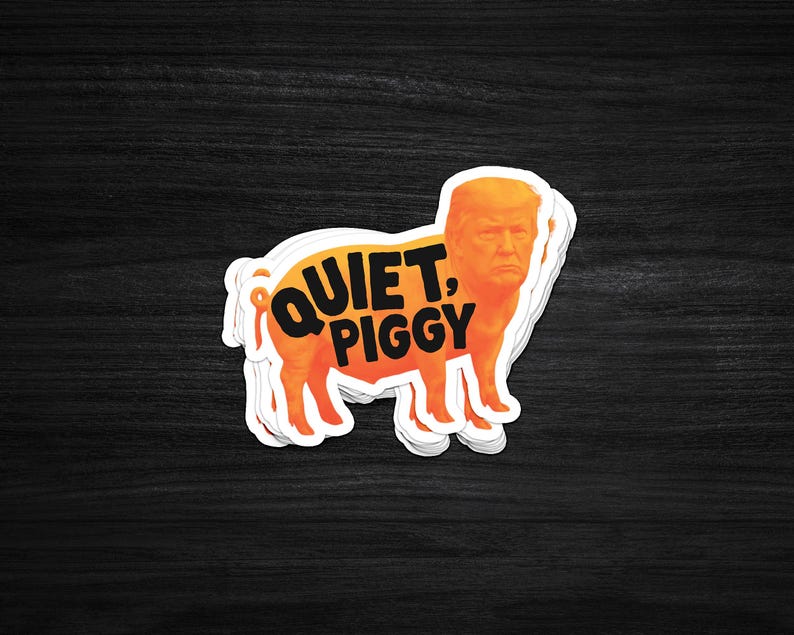 Pode incluir: Um autocolante com um porco laranja com o rosto de um homem. O texto "QUIET, PIGGY" est&aacute; impresso em laranja no corpo do porco. O autocolante tem uma borda branca e est&aacute; colocado sobre uma superf&iacute;cie de madeira escura.