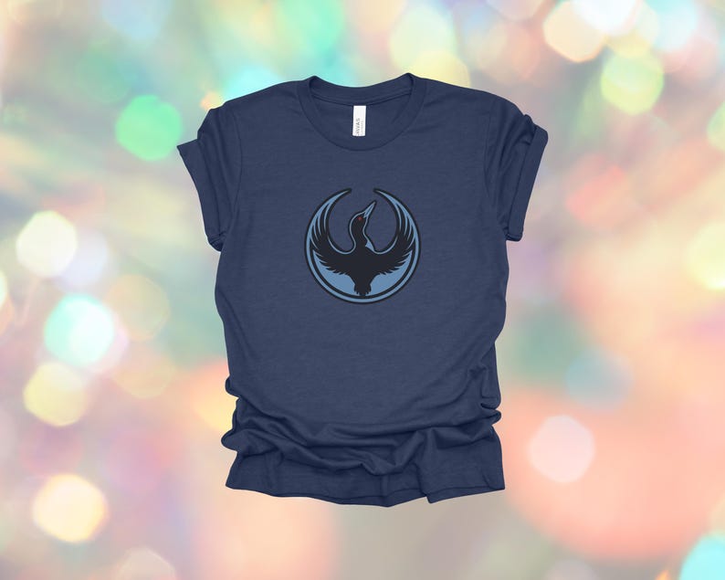 May include: Navy blue t-shirt featuring a circular design with a black bird silhouette inside a light blue circle. The bird is depicted with outstretched wings. The shirt is made of a soft material.